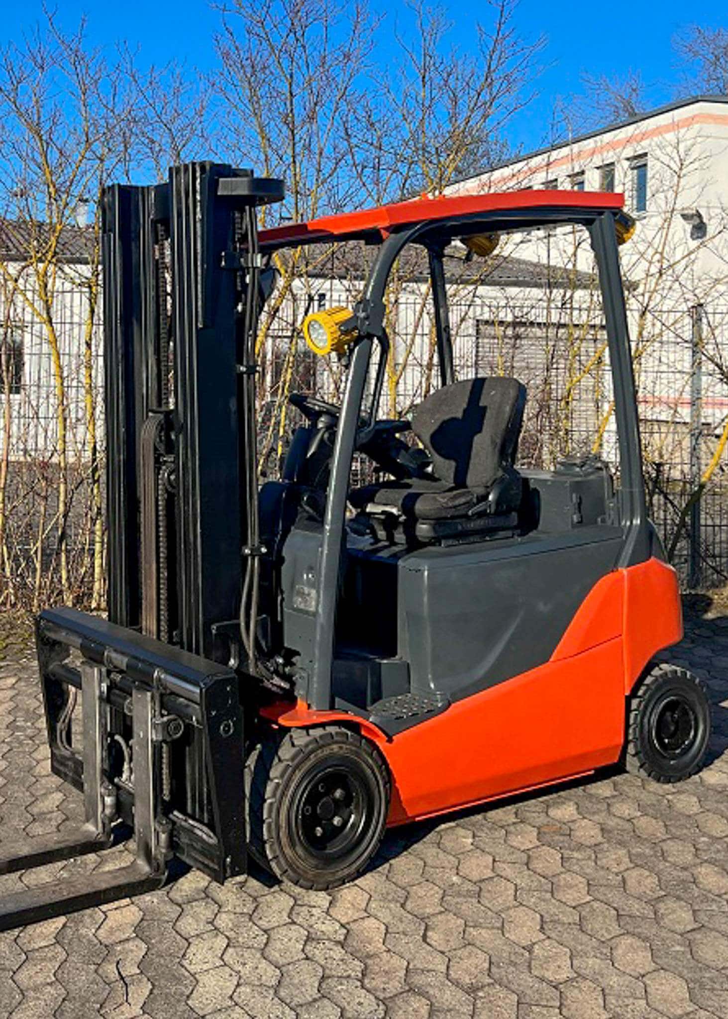 Roter Gabelstapler steht im Freien auf gepflastertem Boden, bei sonnigem Wetter.