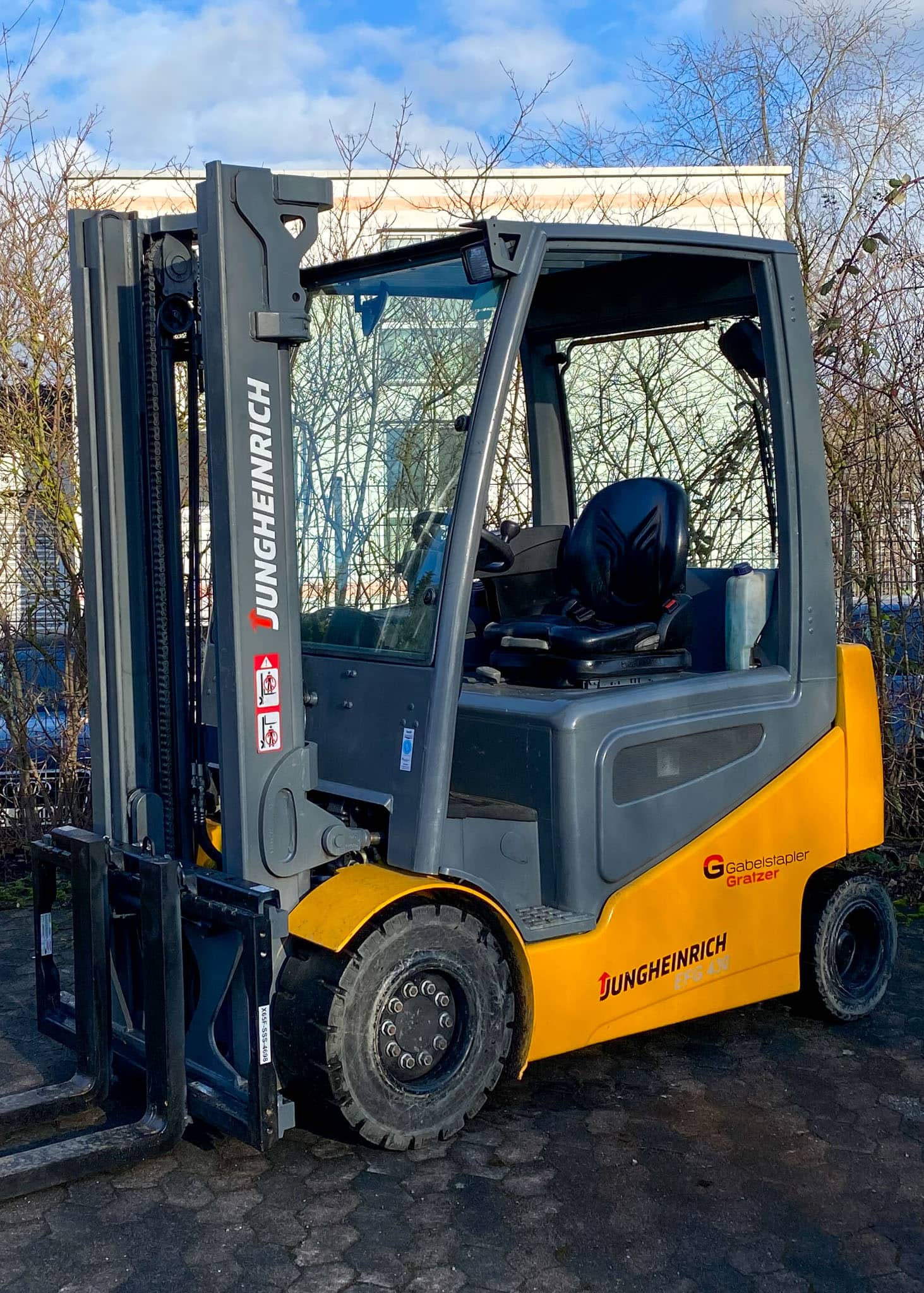 Gelber Jungheinrich-Gabelstapler auf Parkplatz, sonniger Tag, Hebevorrichtung nach oben ausgerichtet.