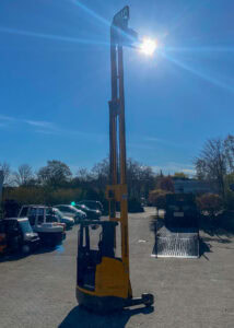 Ein gelber Gabelstapler im Sonnenlicht, auf einem Parkplatz, mit klarem blauen Himmel im Hintergrund.