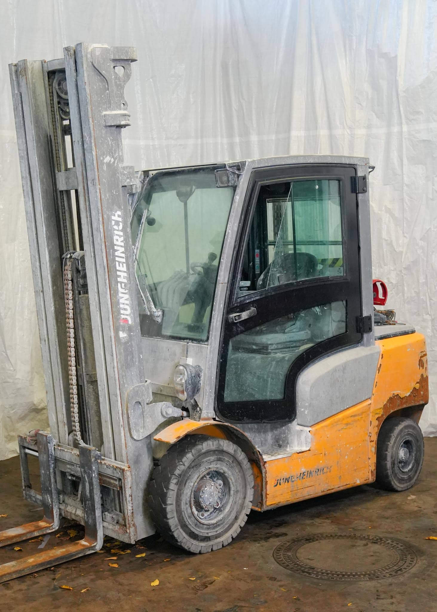 Ein Gabelstapler in Grau und Orange mit sichtbaren Gebrauchsspuren auf Betonboden.